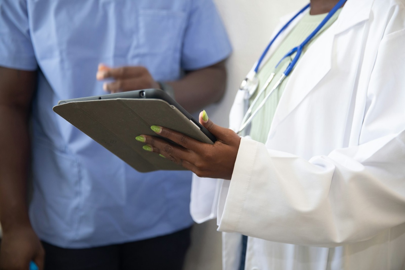 A clinician in a white coat reviews information on a tablet with a colleague