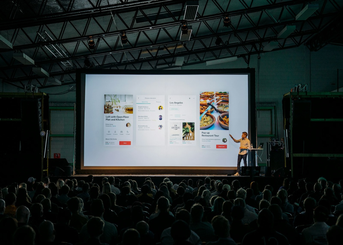 A presenter on stage in front of a large screen and an audience